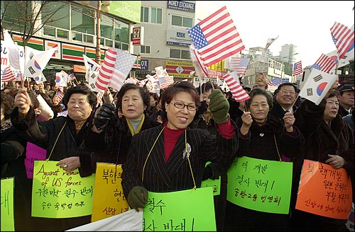 8일 경기도 오산 미공군기지앞에서 '송탄2동 번영회' '송탄 숙박업지부' '송탄 다방업지부' '송탄 미용업지부' 명의의 피켓을 목에 건 시민들이 성조기와 태극기를 흔들고 있다. 